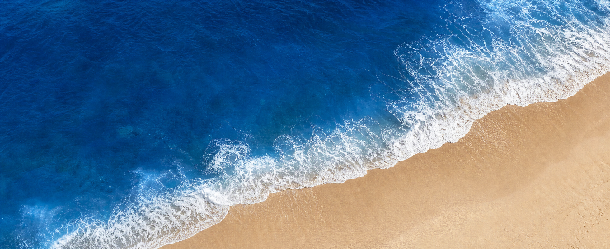 Aerial view of deep cobalt blue waves washing onto a quiet shore