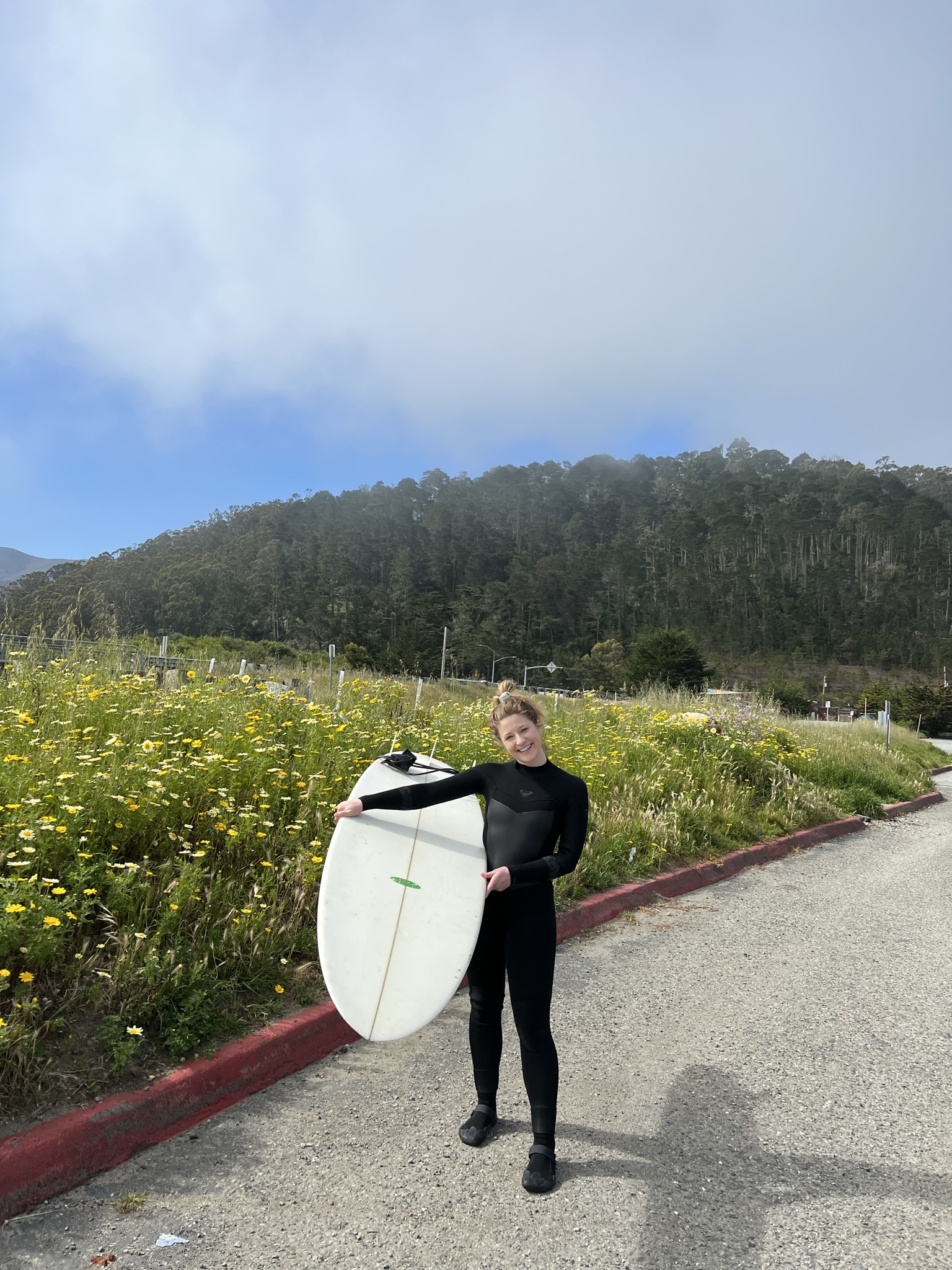 Sarah Joan Fox holding a surfboard near coastal flowers